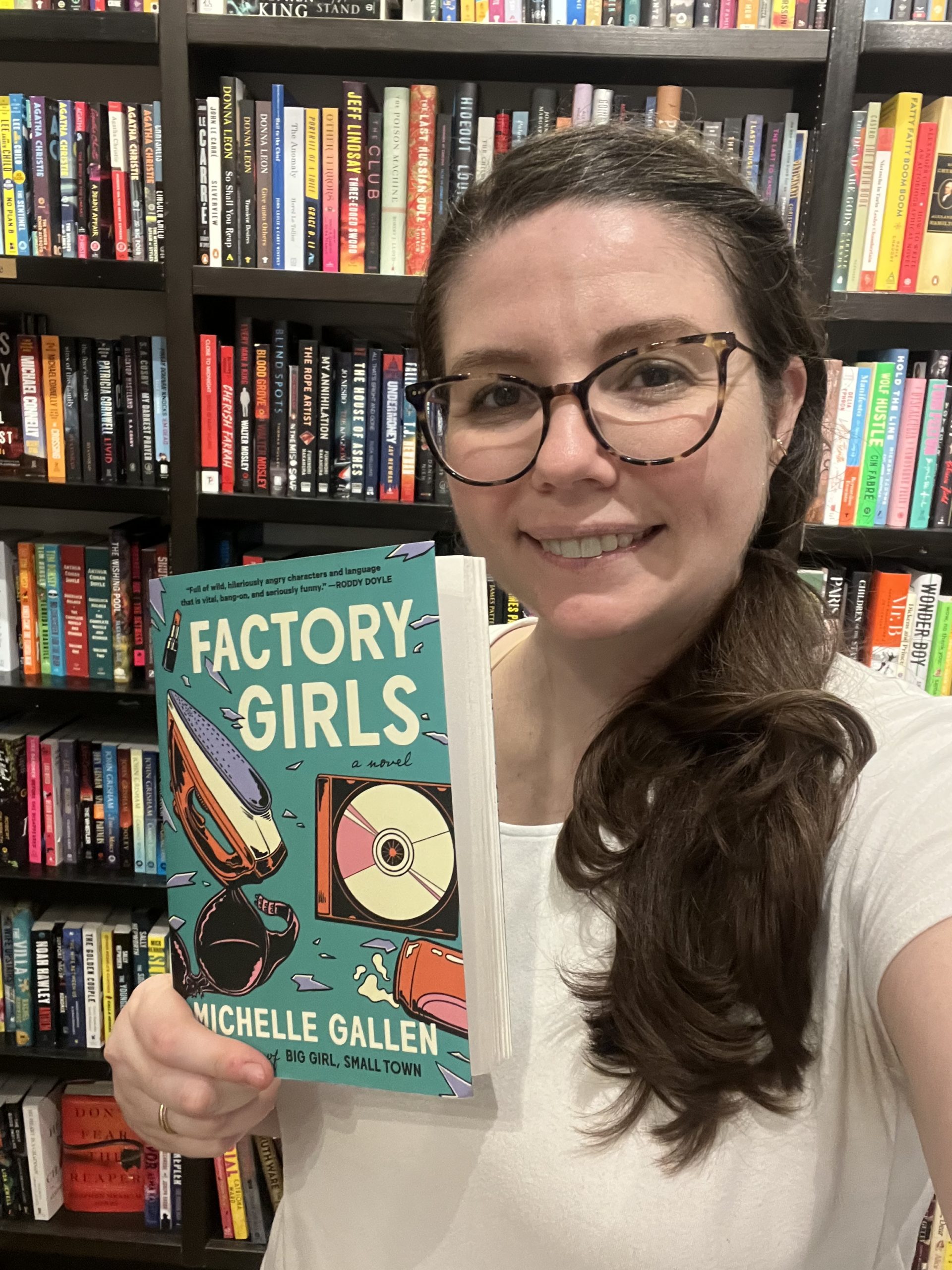 Store manager Emily with the featured staff pick for July, Factory Girls by Michelle Gallen